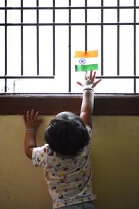 Rear view of baby girl touching indian flag on window