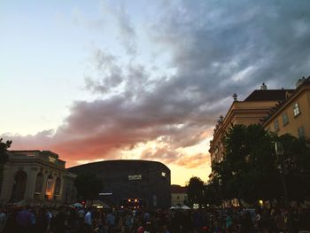 People walking on city street against cloudy sky