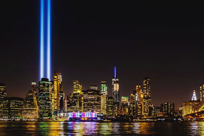 Illuminated buildings by river against sky at night