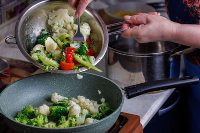 Senior caucasian woman pours vegetables into frying pan out from stainless steel colander