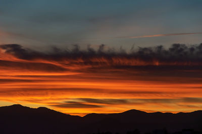 A close up of fire coloured clouds during sunset with a mountain range silhouette below