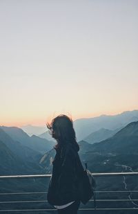 Side view of woman standing against mountains at observation point during sunset
