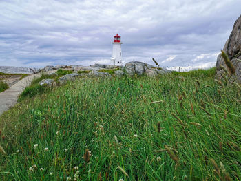 Lighthouse amidst plants and buildings against sky