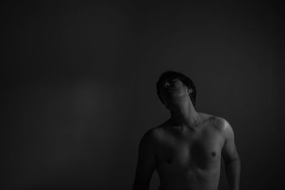 Shirtless man standing against black background