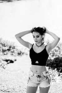 Young woman with hands in hair standing at beach during sunny day