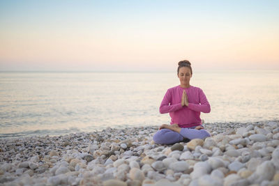 Side view of woman standing at beach against sky during sunset