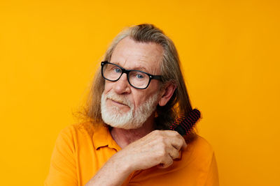 Senior man combing hair against yellow background