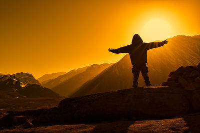 Rear view of man standing on mountain against sky during sunset