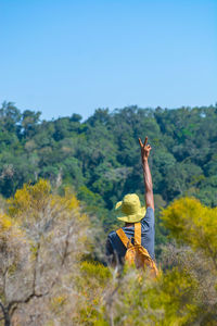 Rear view of a man standing on in the forest against clear sky showing peace sign