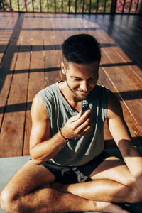 Smiling man smelling aroma oil bottle while sitting cross-legged at at wellness resort