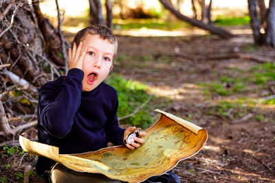 Portrait of boy holding compass and map on land
