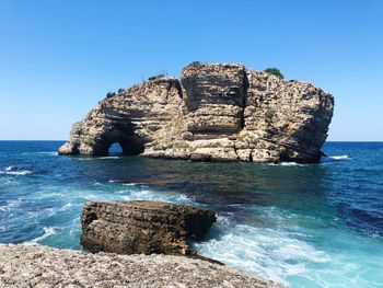 Rock formation in sea against clear blue sky