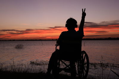 Rear view of man with wheelchair on beach against sky during sunset