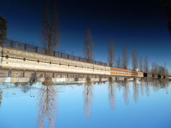 Reflection of bridge in lake against clear blue sky