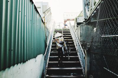 Person with bicycle walking on staircase against sky