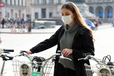 Young woman wearing mask holding bicycle standing outdoors