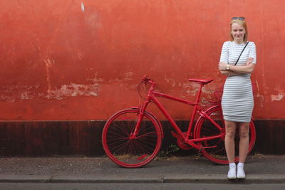 Portrait of young woman standing by bicycle against wall