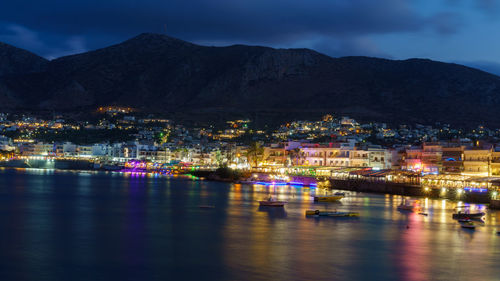 Illuminated buildings by sea against sky at night