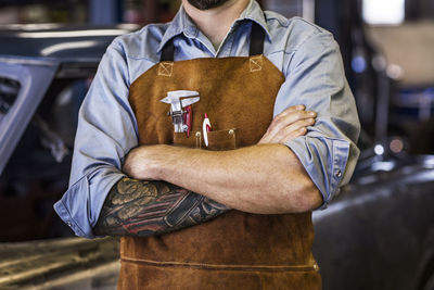 Midsection of mechanic standing with arms crossed in auto repair shop