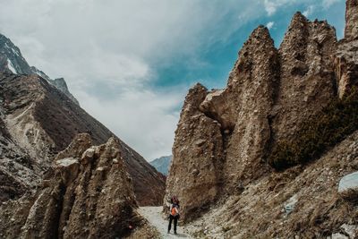 Man standing on footpath by rock formation against sky