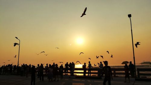 Silhouette people flying at beach against sky during sunset