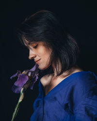 Close-up of woman holding purple flower against black background