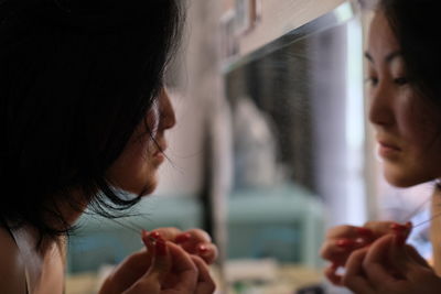 Close-up of woman with black hair looking in mirror at home