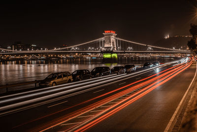 Light trails on bridge over road against sky at night