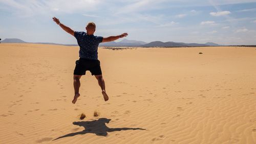 Man jumping on sand at beach against sky