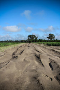 Tire tracks on sand against blue sky