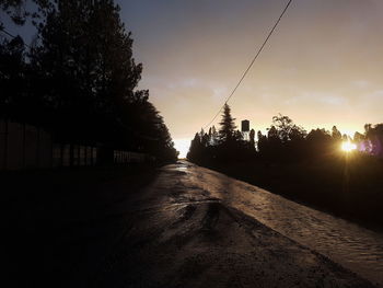 Road amidst silhouette trees against sky during sunset