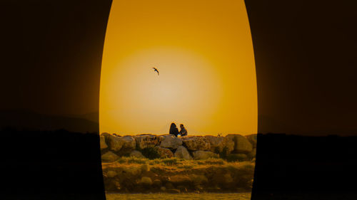 Silhouette people on rock against sky during sunset