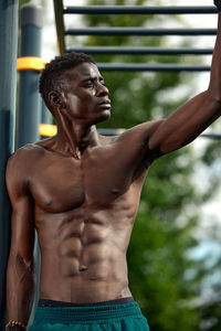 Portrait of shirtless man standing against trees