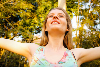 Close-up of smiling young woman with arms outstretched at park