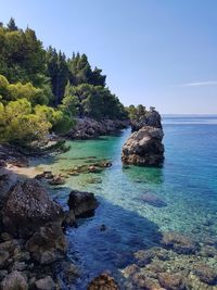 Scenic view of rocks in sea against clear blue sky