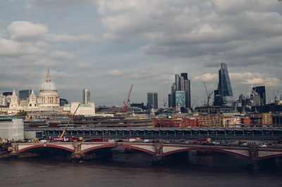 Bridge over river in city against cloudy sky