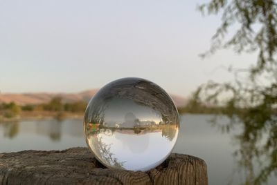 Upside down image of crystal ball by lake against sky