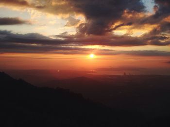 Scenic view of landscape against cloudy sky at sunset