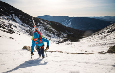 Climber ascending mountain with tools and skis in the white mountains