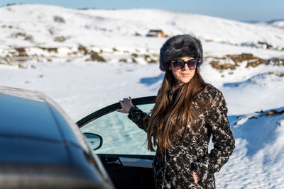 Portrait of woman standing by car on snow covered land