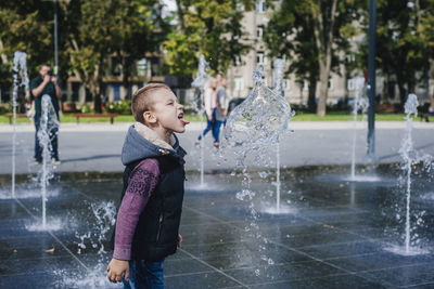 Boy sticking out tongue while standing in fountain