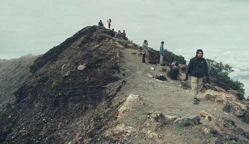 People on rock by mountain against sky