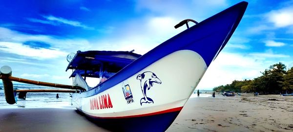 Close-up of boat moored on beach against blue sky