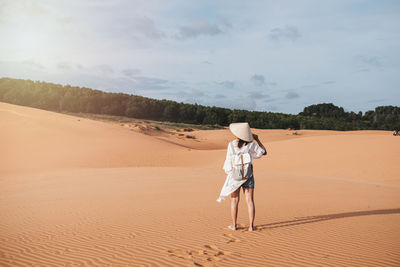 Rear view of boy on sand dune in desert against sky