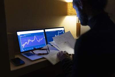 Businessman with documents analyzing stock market data on laptop at home office