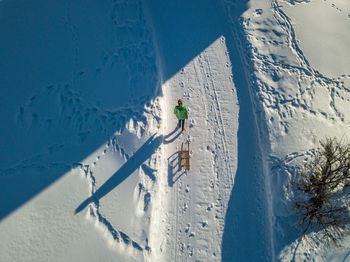 High angle view of woman pulling sleigh while walking on snow covered land
