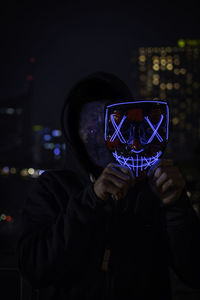Digital composite image of man holding illuminated mask at night