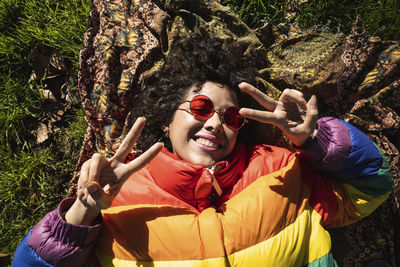 Smiling woman showing peace sign while lying on grass at park