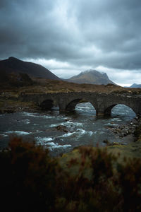 Arch bridge over river against cloudy sky