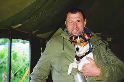 Portrait of smiling man with jack russell terrier standing in tent at campsite